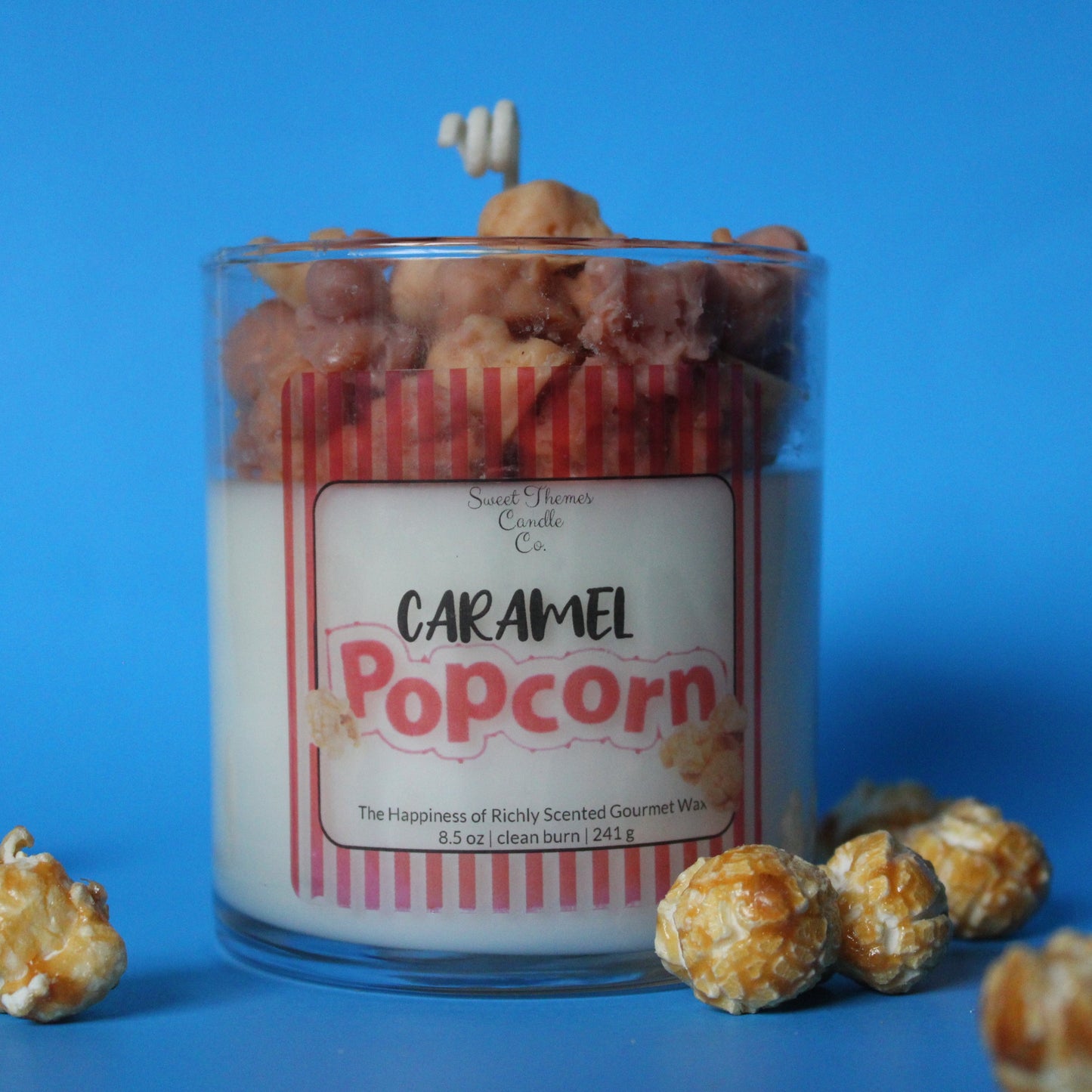 Caramel popcorn candle with popcorn kernels on a blue background