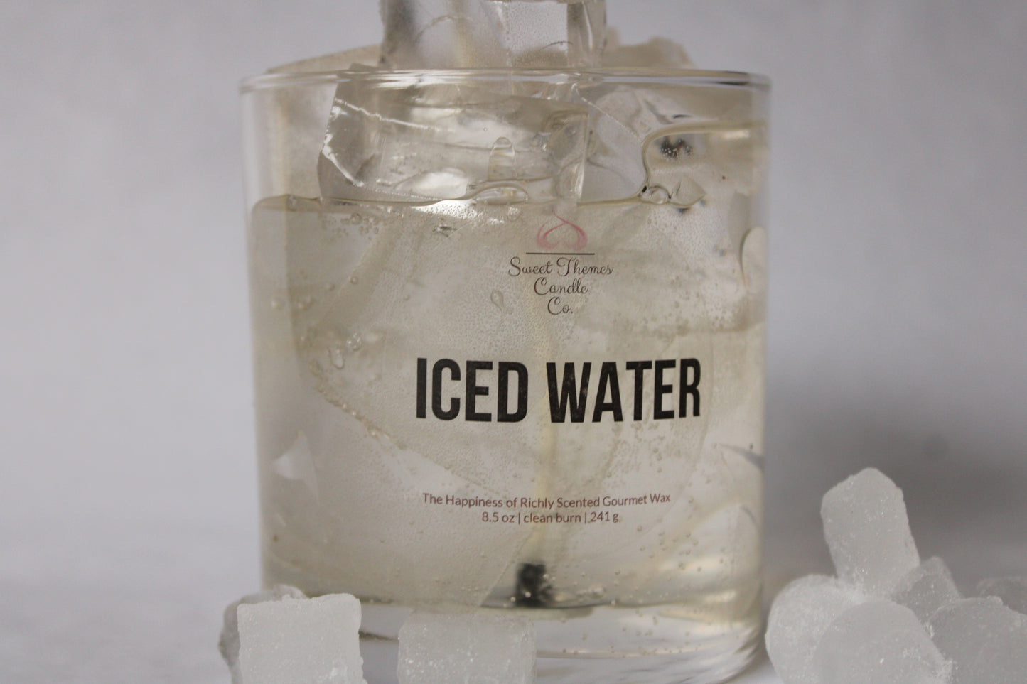 Candle labeled 'ICED WATER' with ice cubes around it on a light background