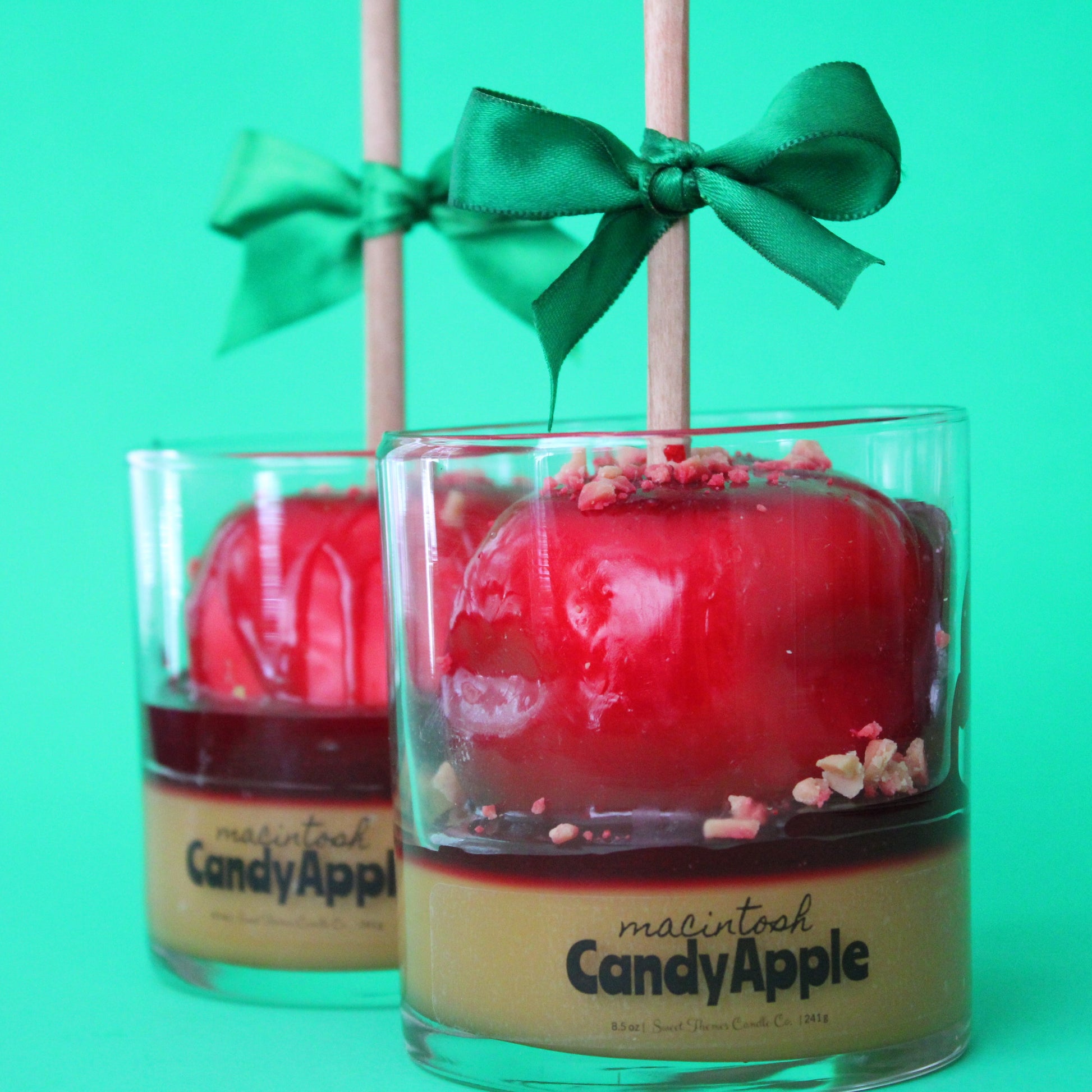 Two red candy apples in glass containers with green bows on a green background