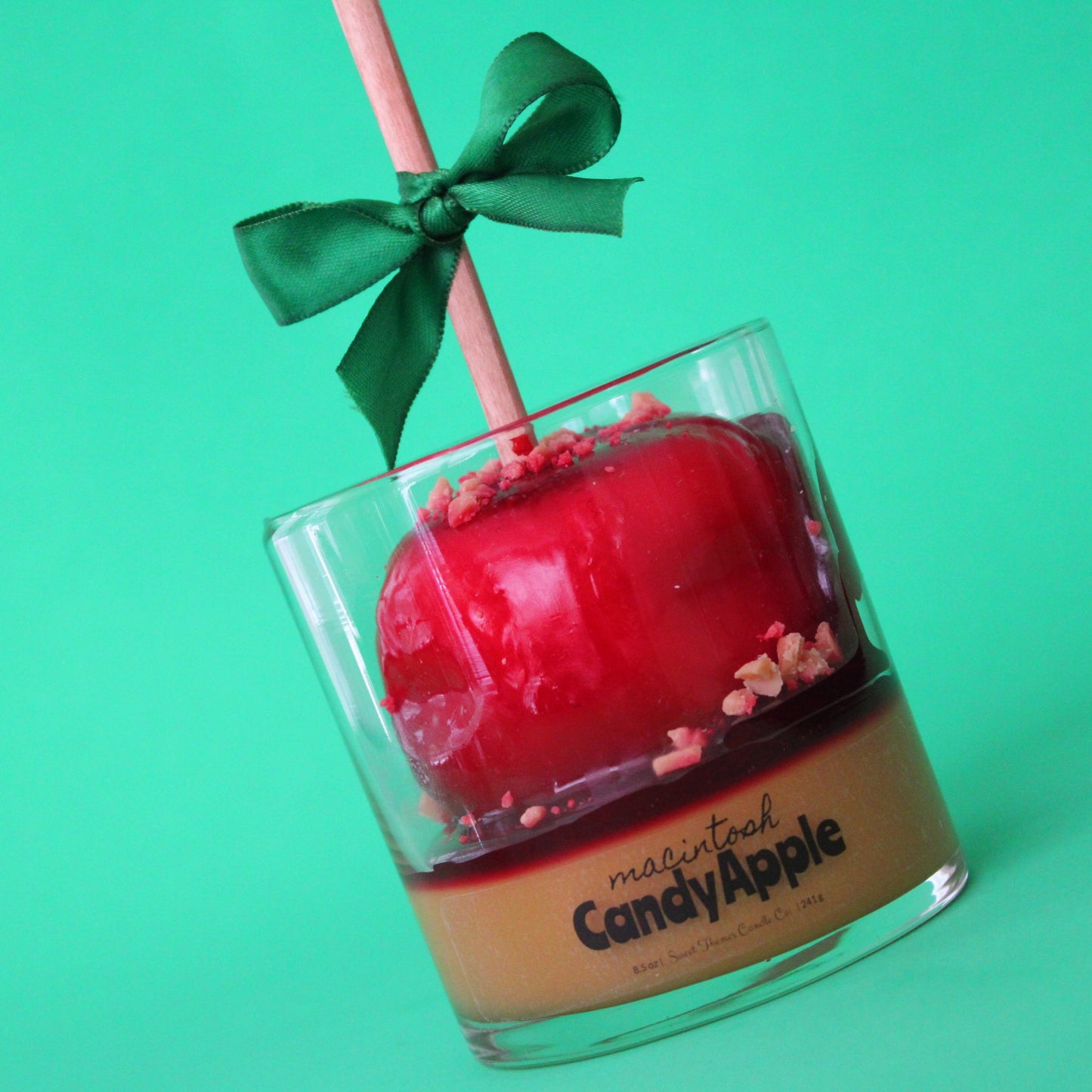Red candy apple in a glass container with a green bow on a green background