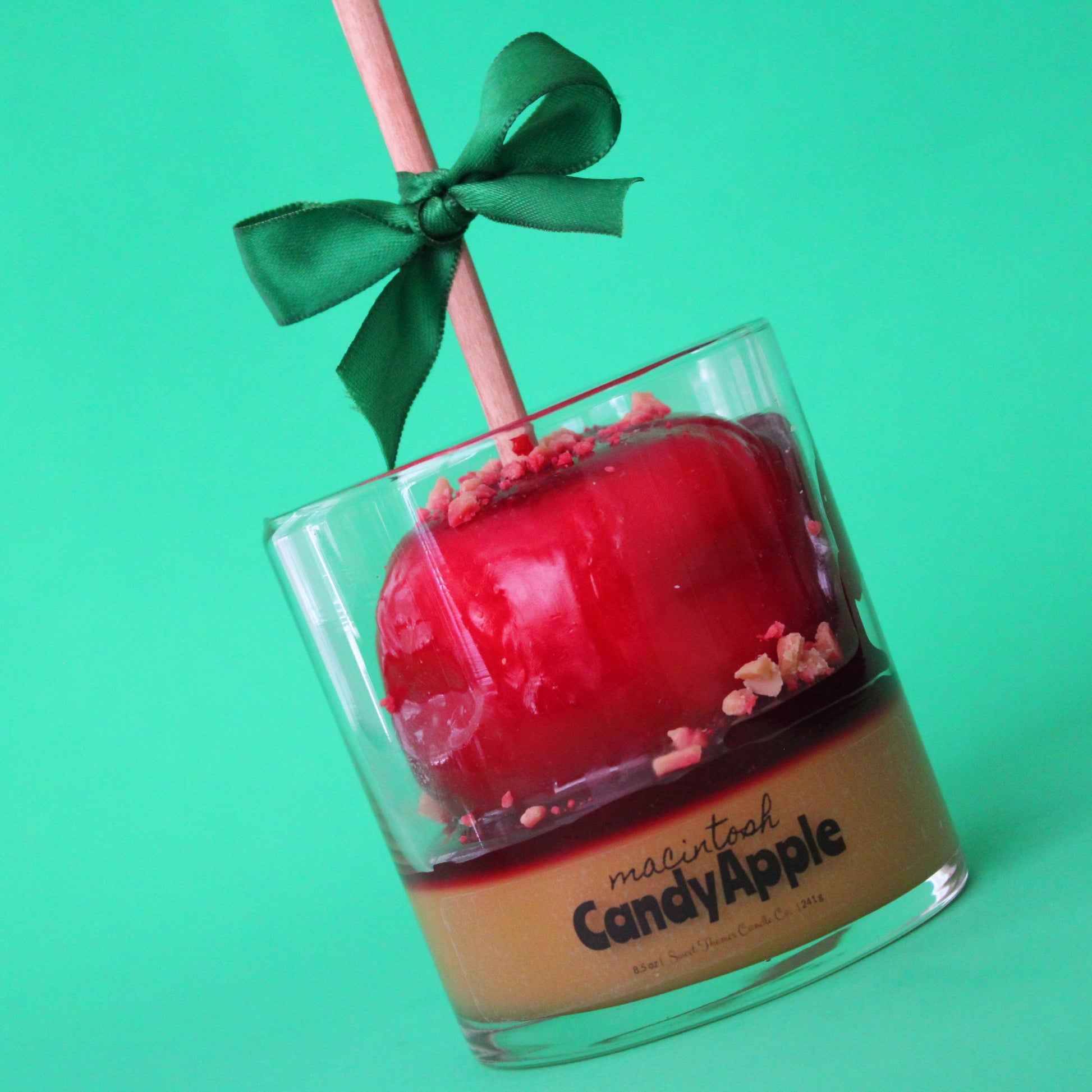 Red candy apple in a glass container with a green bow on a green background
