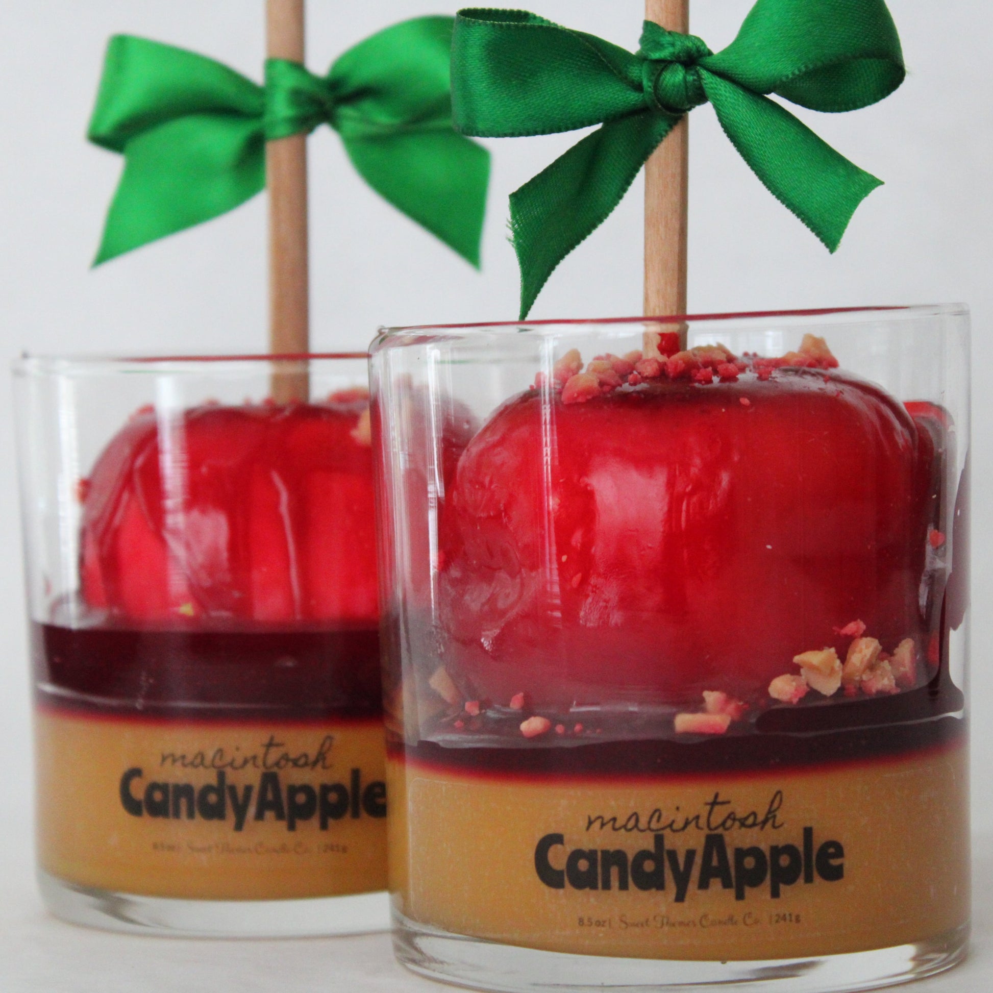 Two glass containers with red candy apples and green bows on a white background