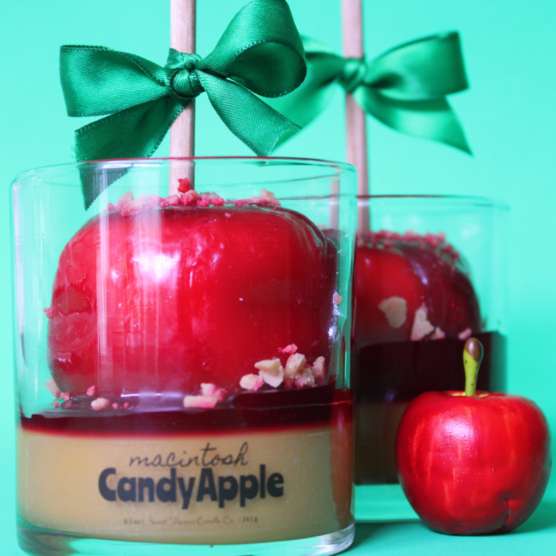 Red candy apple in a glass with a green bow on a teal background