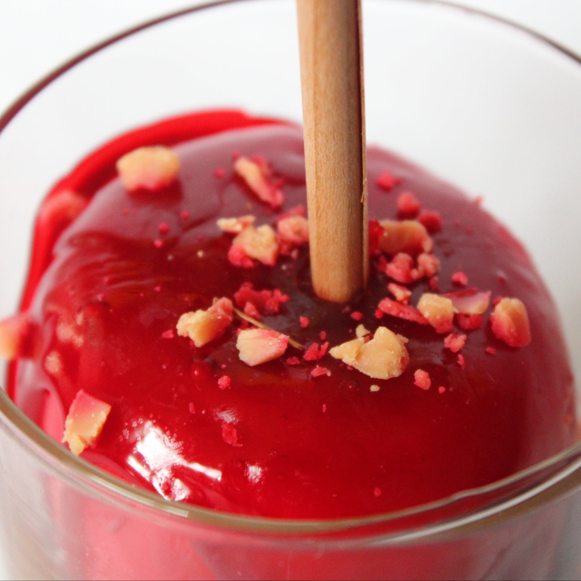 Red candy apple in a glass with a stick on a white background